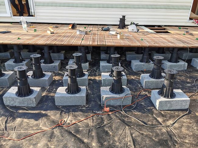 Plots soporte regulables de terraza montados sobre bloques de hormigón que sostienen una estructura de terraza de madera.