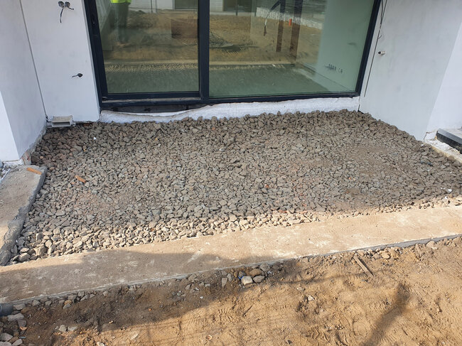 Capa de piedra triturada preparada para la construcción de una terraza en el exterior frente a puertas correderas de cristal.