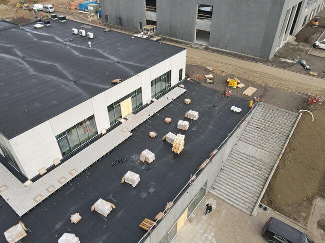 Vista aérea de la azotea plana de un edificio en construcción con baldosas de terraza y plots soporte siendo instalados.