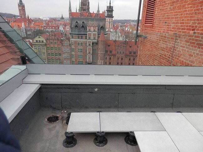 Instalación de baldosas elevadas apoyadas sobre plots soporte regulables de plástico en una terraza en la azotea.