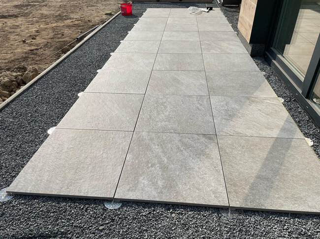 Baldosas de porcelana gris claro instaladas sobre plots soporte de terraza regulables de baja altura sobre una base de grava.
