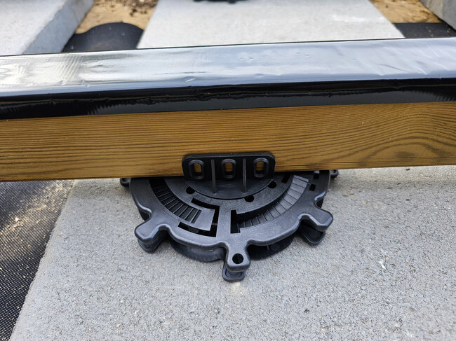 Primer plano de un plots soporte regulable de plástico que sostiene una viga de madera de terraza.