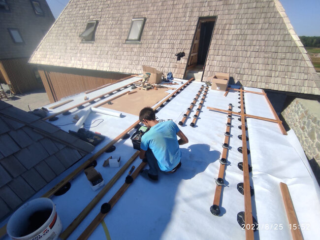 Contratista instalando plots soporte regulables y vigas de madera sobre una membrana de cubierta plana.