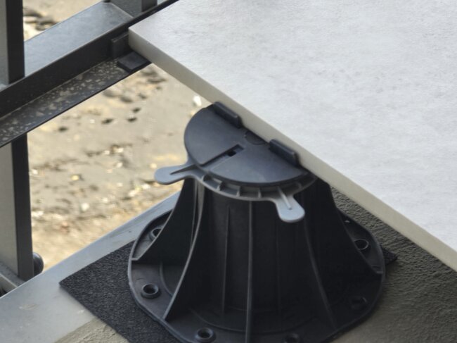 Plot soporte regulable que sostiene el borde de una baldosa porcelánica exterior en un balcón.