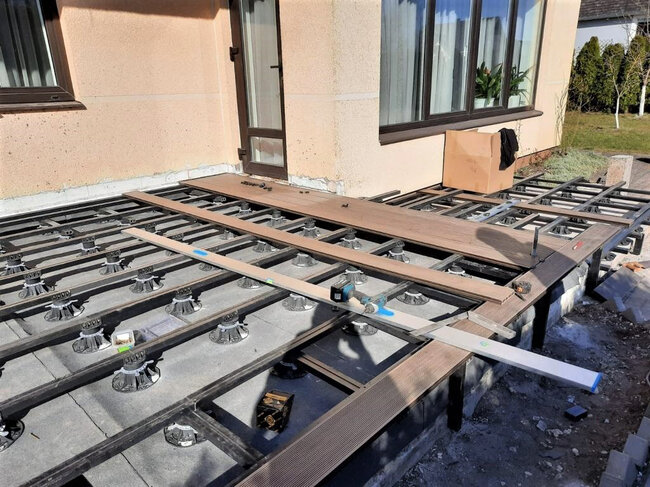 Instalación de tablas de tarima compuesta sobre una subestructura de vigas soportada por plots soporte regulables.